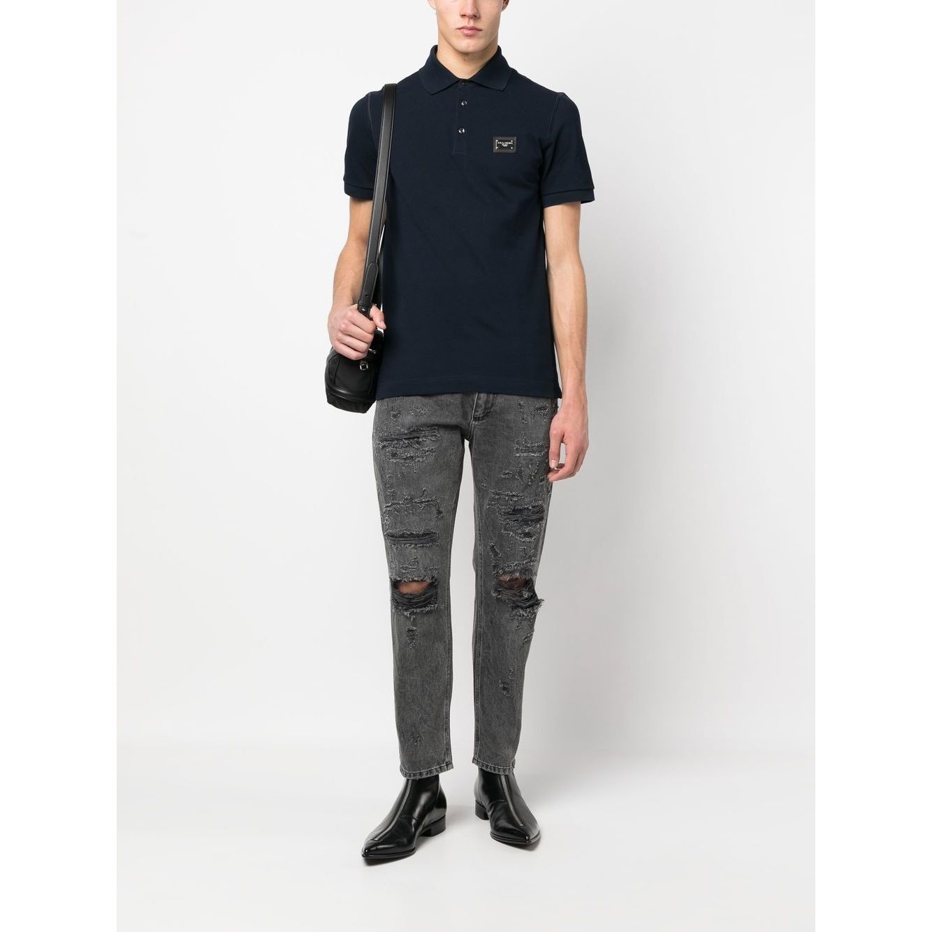 Man wearing navy blue Dolce & Gabbana Logo cotton polo shirt with ribbed trim, logo patch, and short sleeves, paired with distressed jeans.