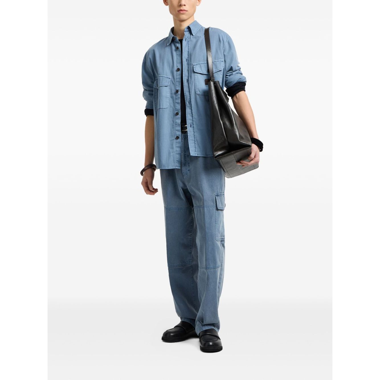 Person wearing denim shirt and pants with black boots, carrying a black bag.