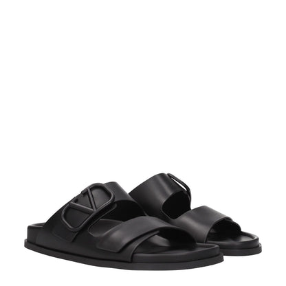Valentino Garavani Black Leather Slippers with open toe and front logo detail, featuring low flat heel and rubber sole.