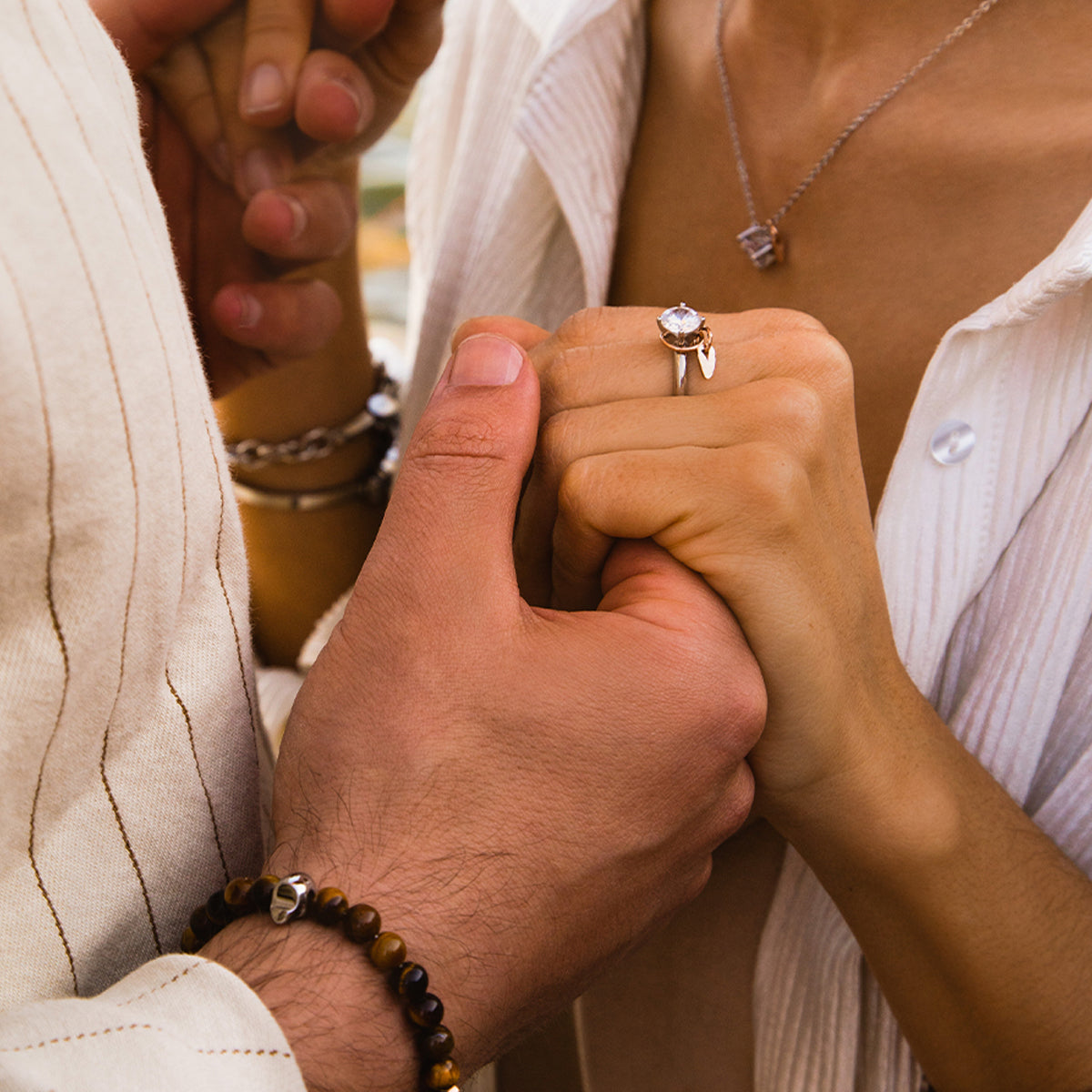 Couple holding hands featuring AN JEWELS JEWELRY Mod. AA.P255RBR ring and necklace, showcasing elegant design and craftsmanship.
