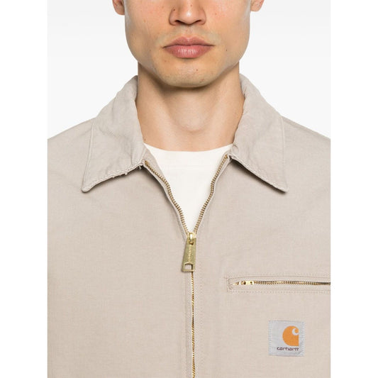 Man wearing CARHARTT WIP MAIN Jackets Beige with zip fastening and chest pocket, showing front design.