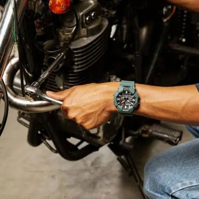 Person wearing CASIO G-SHOCK Mod. NEW RUGGED BASIC Analog-Digital 10-Year Battery wristwatch while working on a motorcycle.