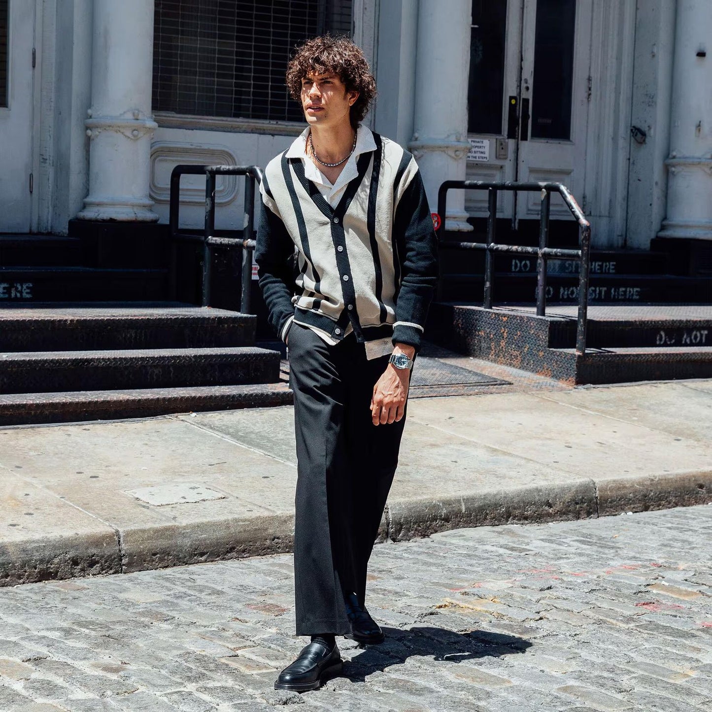 Man wearing a stylish black and white outfit walking on a cobblestone street.