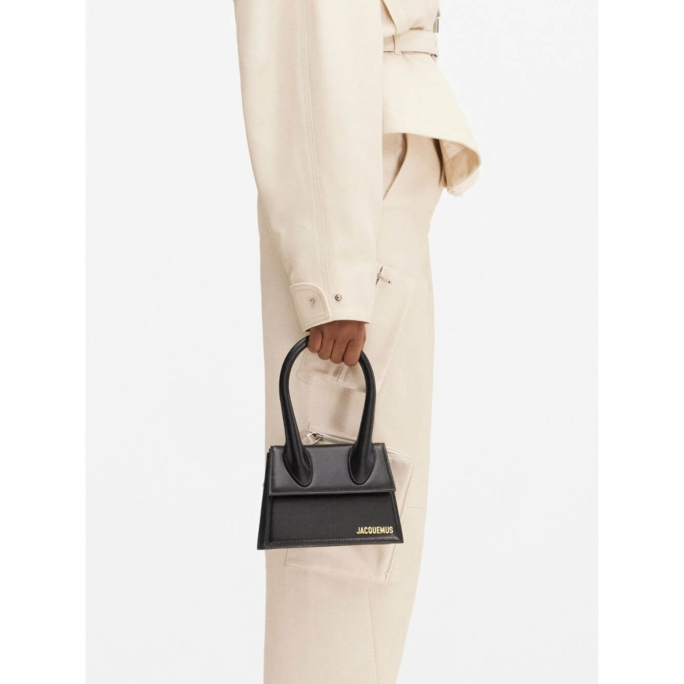 Jacquemus Le Chiquito Moyen Black Bag with gold hardware, magnetic flap, and removable shoulder strap on model's hand.