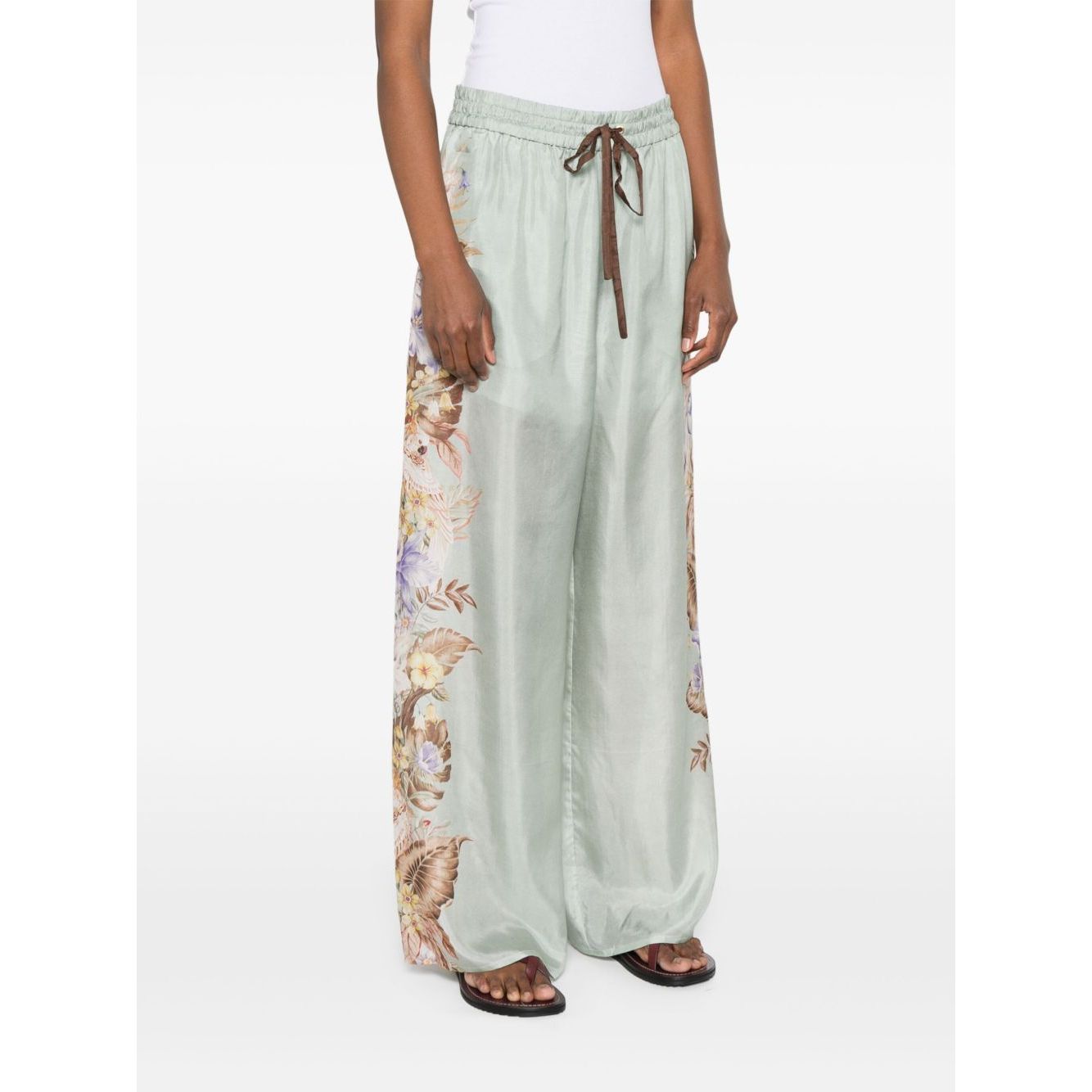 Woman wearing Zimmermann Coco trousers featuring a sage green floral print with elasticated drawstring waistband and side pockets.
